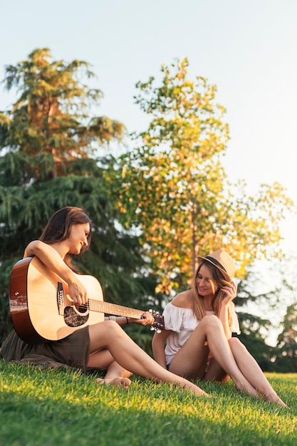 Belle donne che si divertono a suonare la chitarra nel parco. Amici e concetto di estate.