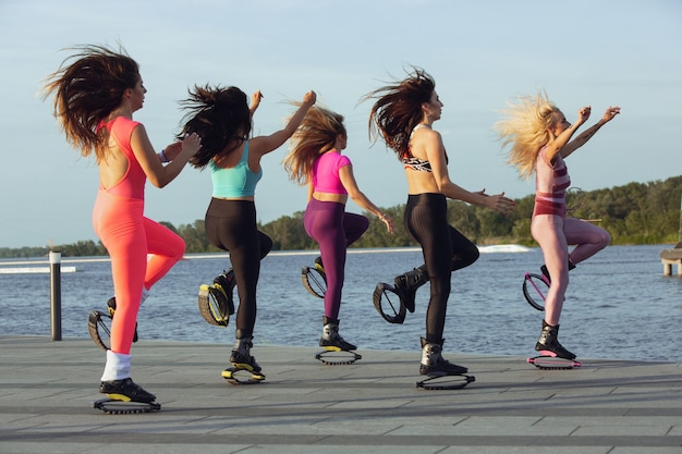 Belle donne in abbigliamento sportivo che saltano in un kangoo salta le scarpe per strada in una giornata di sole.