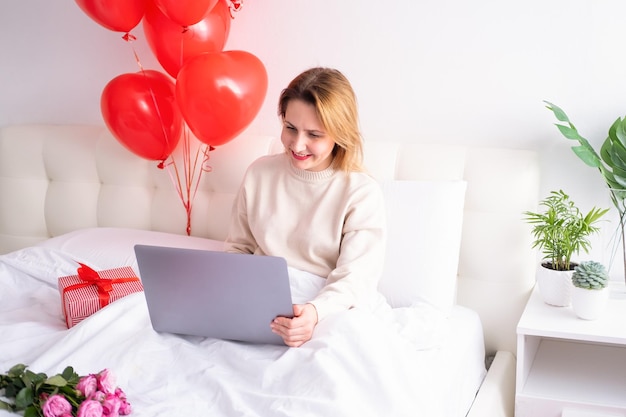 Belle donne in abiti casual e accoglienti utilizzando il computer portatile sul letto per celebrare il giorno di San Valentino