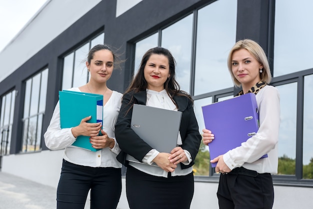 Belle e giovani donne d'affari con documenti e cartelle in posa all'esterno dell'edificio per uffici