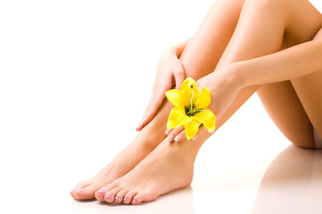 Belle gambe ben curate della ragazza con un fiore giallo in mano su uno sfondo bianco