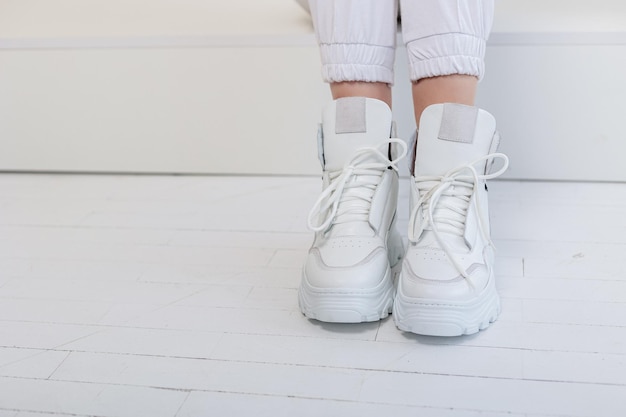 Belle gambe femminili in pantaloni bianchi, scarpe da ginnastica in pelle bianca. Nuova collezione di scarpe casual da donna