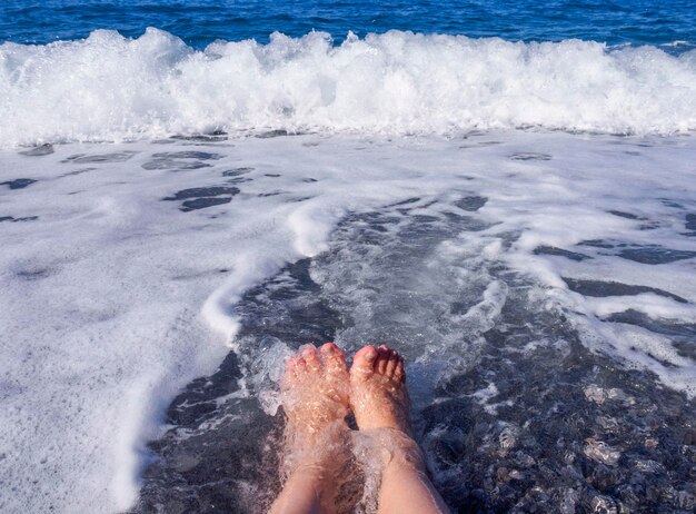 Belle gambe femminili nella schiuma dell'acqua di mare nel Mar Egeo in una giornata di sole in Grecia