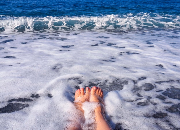 Belle gambe femminili nella schiuma dell'acqua di mare nel Mar Egeo in una giornata di sole in Grecia