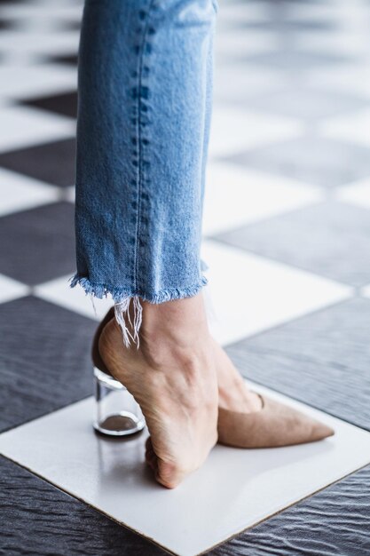 Belle gambe femminili sottili e snelle in jeans con tacchi alti beige Un piede è sulla punta del pavimento Gambe di donna su un pavimento a scacchiera