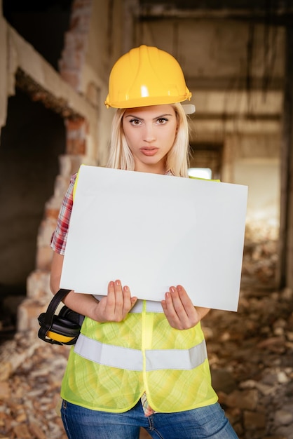 Belle giovani architetti edili femminili che tengono un bordo bianco in bianco nell'edificio danneggiato nel disastro.