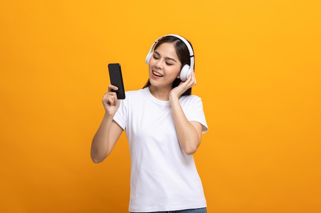 Belle giovani donne asiatiche scelgono la canzone e ascoltano musica dalla connessione smartphone con cuffie wireless divertendosi. L'adolescente ascolta la musica e si rilassa su uno sfondo giallo isolato.