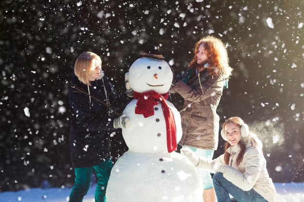 Belle giovani donne che si divertono a costruire un pupazzo di neve in una giornata invernale nevosa in un parco