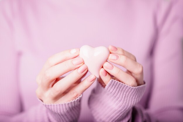 Belle mani femminili che tengono cuore rosa in ceramica