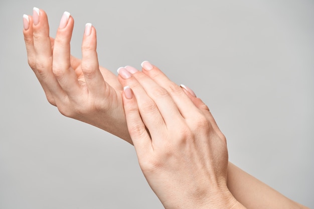 Belle mani femminili con french manicure su superficie grigio chiaro