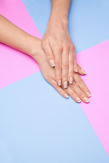 Belle mani femminili con french manicure sulla superficie della carta colorata