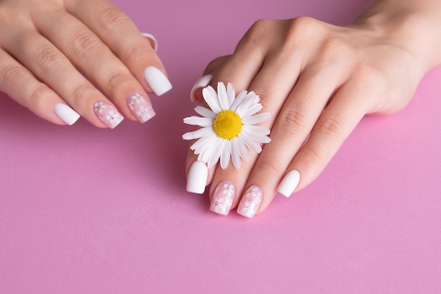 Belle mani femminili con unghie manicure rosa e bianche disegno floreale