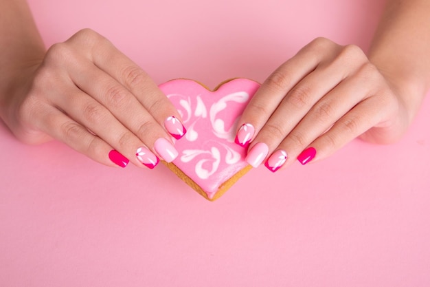 Belle mani femminili con unghie manicure rosa fiori design tenendo caramelle a forma di cuore