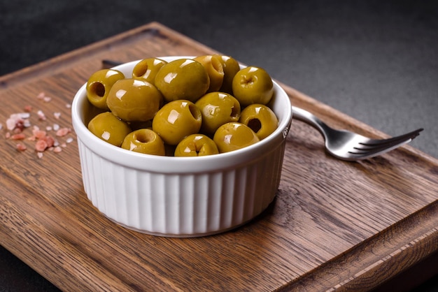 Belle olive verdi in salamoia su uno sfondo di cemento scuro. Preparazione della tavola festiva