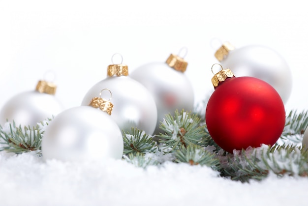 Belle palle bianche e rosse di Natale con il ramo e la neve dell'abete su fondo bianco