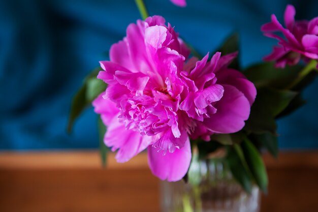 Belle peonie rosa in un vaso di vetro sono in piedi su un vassoio di legno nel letto. Avvicinamento.