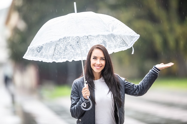 Belle ragazze sorridenti con un ombrello controllano con la mano se sta ancora piovendo.