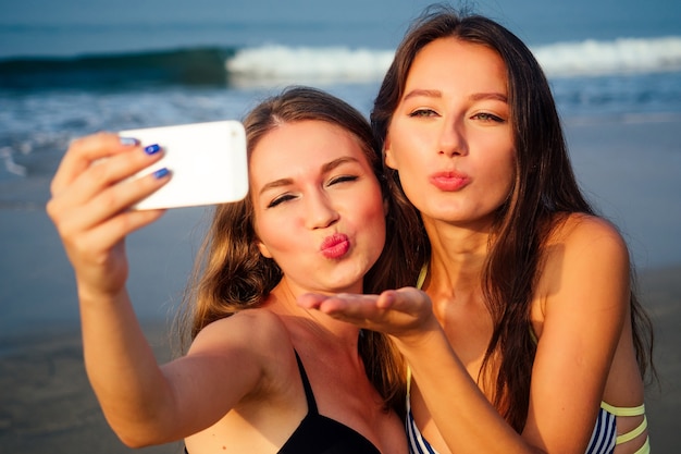 Belle ragazze sulla spiaggia fanno selfie sul bacio d'aria del telefono.