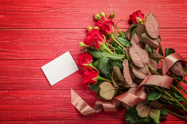 Belle rose rosse con carta su fondo di legno