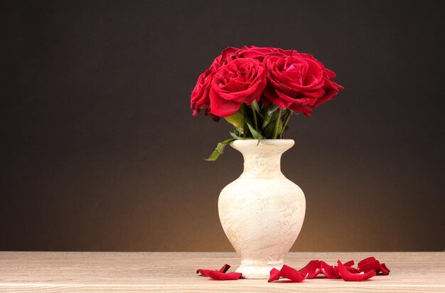 Belle rose rosse in vaso sulla tavola di legno su fondo marrone