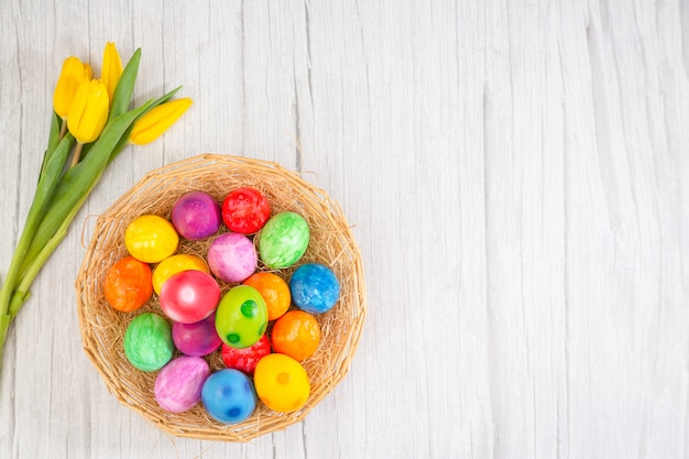 Belle uova di Pasqua del gruppo in primavera del giorno di pasqua, uova rosse, blu, porpora e gialle in canestro di legno con i tulipani sulla tavola di legno