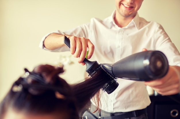 bellezza, acconciatura, phon e concetto di persone - primo piano di donna e parrucchiere con ventola e spazzola che fanno uno styling caldo al parrucchiere