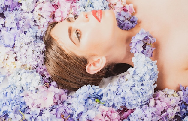 Bellezza Donna sdraiata sui fiori. Cosmetici e cura della pelle per il trucco Blossom. Ragazza con fiori di ortensia.