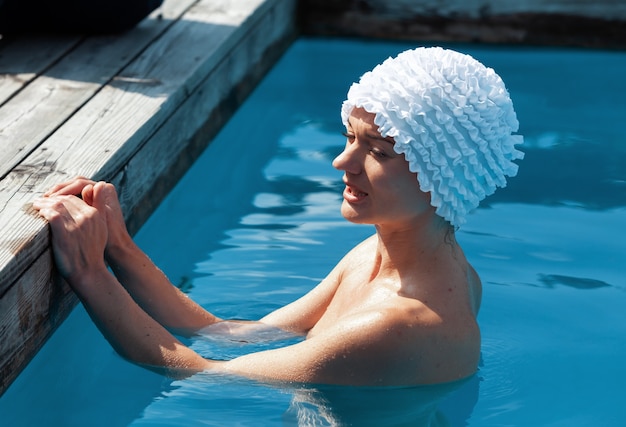 Bellezza e concetto di stile di vita sano. Bella giovane donna nuda in piscina. La giovane donna nuda si diverte a nuotare in piscina