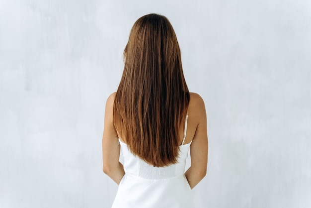 Bellezza e cura dei capelli. Punto di vista posteriore di giovane signora castana sensuale con la posa voluminosa dei capelli isolata su bianco e mostrando i suoi capelli sani. Foto d'archivio