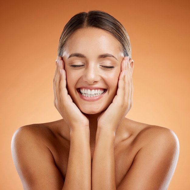 Bellezza e donna per la cura della pelle entusiaste del trucco del viso sullo sfondo dello studio arancione mockup Sorriso felice e modello di ragazza giovane con cosmetici per il viso e benessere dalla dermatologia con spazio mock up