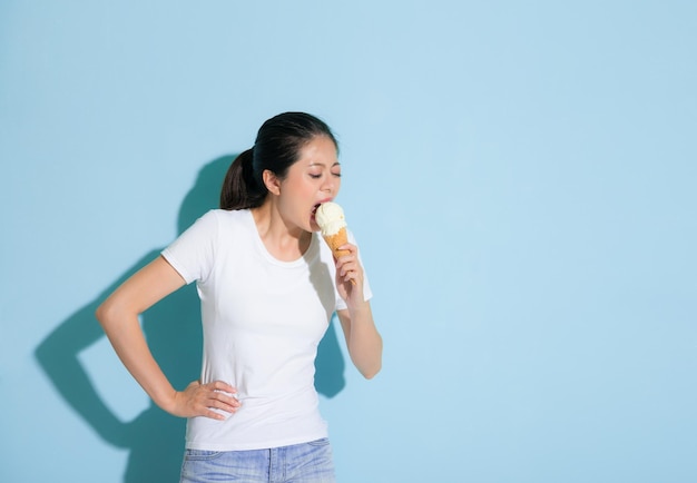 bellezza giovane modello femminile sensibile alla malattia dei denti sfida del paziente a mangiare il gelato tollerare la posizione dolorosa sullo sfondo blu della parete.