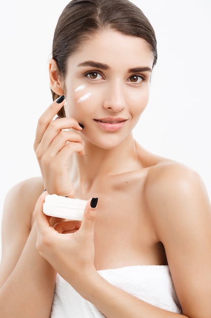 Bellezza Giovani Concetto di cura della pelle - Close up Bella donna caucasica ritratto Applicare una crema al suo volto per la cura della pelle. Bella ragazza modello Spa con perfetta pelle pulita fresca su sfondo bianco.