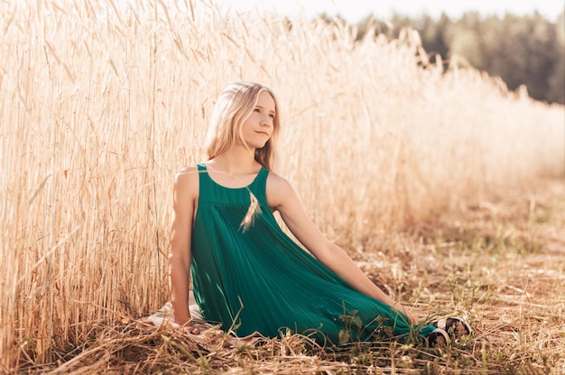 Bellezza Ragazza romantica all'aperto Bella ragazza modello teenager in abito verde sul campo alla luce del sole Soffia lunghi capelli biondi Bagliore del sole Luce del sole Retroilluminazione dai toni caldi