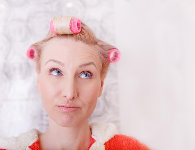 Bellezza ragazza vento i capelli in bigodini Giovane ragazza pensosa pensa a un'acconciatura alla moda sulla sua testa un grande bigodino rosa