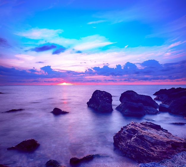 Bellissima alba colorata sul mare con nuvole e massi drammatici. Fondo di viaggio naturale all'aperto del mondo di bellezza