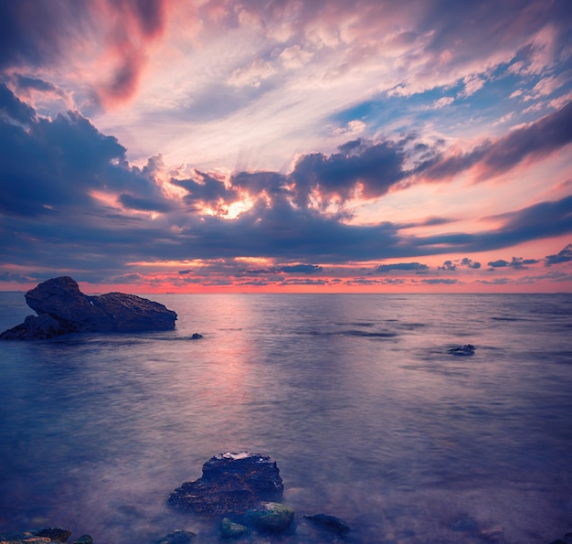 Bellissima alba colorata sul mare con nuvole e massi drammatici. Fondo di viaggio naturale all'aperto del mondo di bellezza