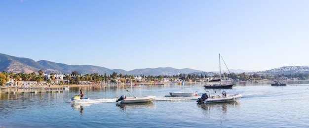 Bellissima baia con acque calme, barche e yacht da spiaggia sabbiosa piccola città e montagne verdi sul