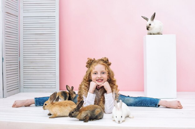 Bellissima bambina con i capelli ricci e con soffici animali conigli su sfondo rosa