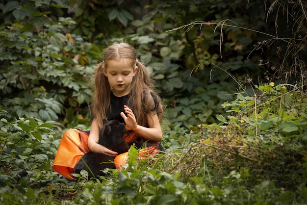 Bellissima bambina con lunghi capelli chiari che indossa un costume da strega che tiene in braccio il suo soffice gatto nero preferito