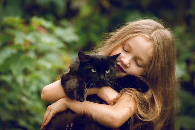 Bellissima bambina con lunghi capelli chiari che indossa un costume da strega che tiene in braccio il suo soffice gatto nero preferito