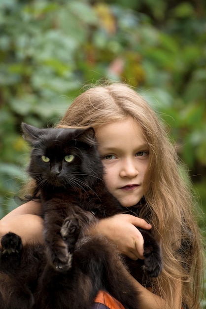 Bellissima bambina con lunghi capelli chiari che indossa un costume da strega che tiene in braccio il suo soffice gatto nero preferito