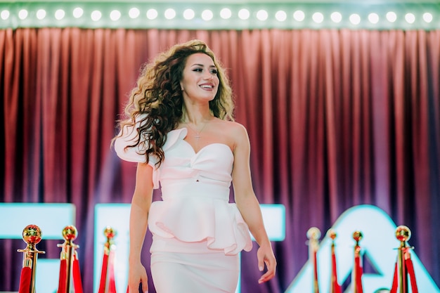 Bellissima e lussuosa ragazza con abito bianco che cammina sul tappeto rosso durante la cerimonia