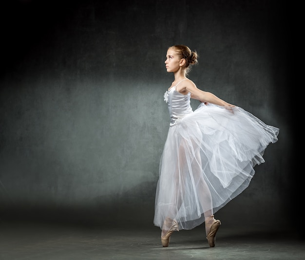 Bellissima giovane ballerina sta ballando in studio su un muro scuro Una piccola ballerina. Ballerino classico.