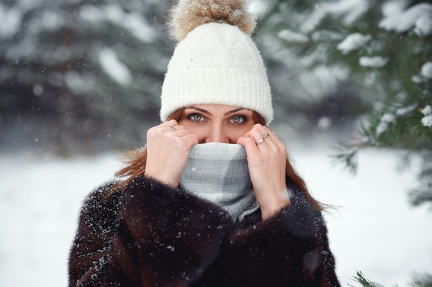 Bellissima giovane donna in abiti invernali a maglia calda copriva il viso con una sciarpa, tenendosi le mani davanti al naso e guardando