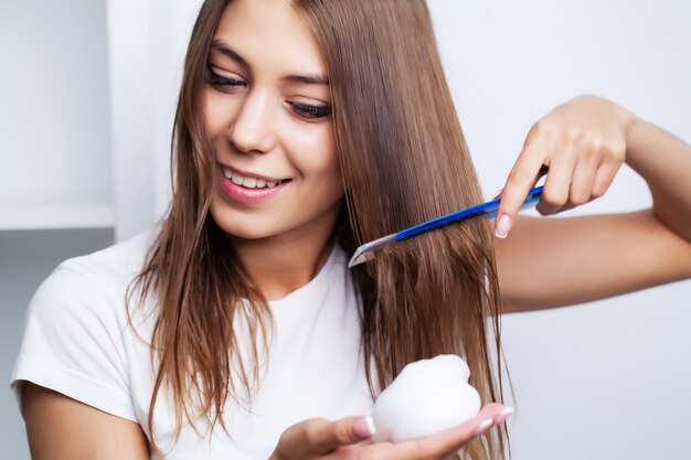 Bellissima giovane donna si prende cura dei suoi capelli, pettinando i capelli lunghi con un pettine