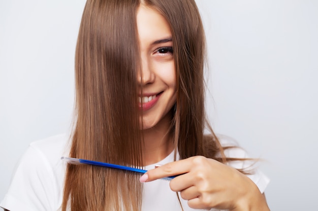 Bellissima giovane donna si prende cura dei suoi capelli, pettinando i capelli lunghi con un pettine