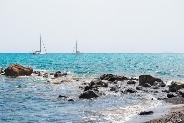 Bellissima spiaggia con acque turchesi e yacht in riva al mare. Isola di Santorini, Grecia.