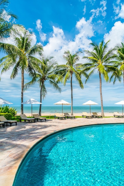 Bellissima spiaggia tropicale e mare con ombrellone e sdraio intorno alla piscina in hotel resort per viaggi e vacanze