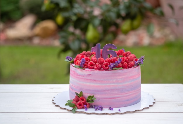 Bellissima torta di compleanno con il numero sedici, decorata con lamponi e fiori di lavanda