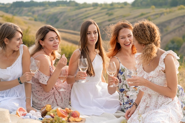 bellissime amiche che si divertono, bevono vino e si godono un picnic nel paesaggio collinare